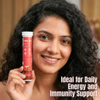 An Indian woman with curly dark hair smiles as she holds a tube of Free On Vitamin C with Iron effervescent tablets. The red tube features illustrations of bubbles and is labeled "Ideal for Daily Energy and Immunity Support."