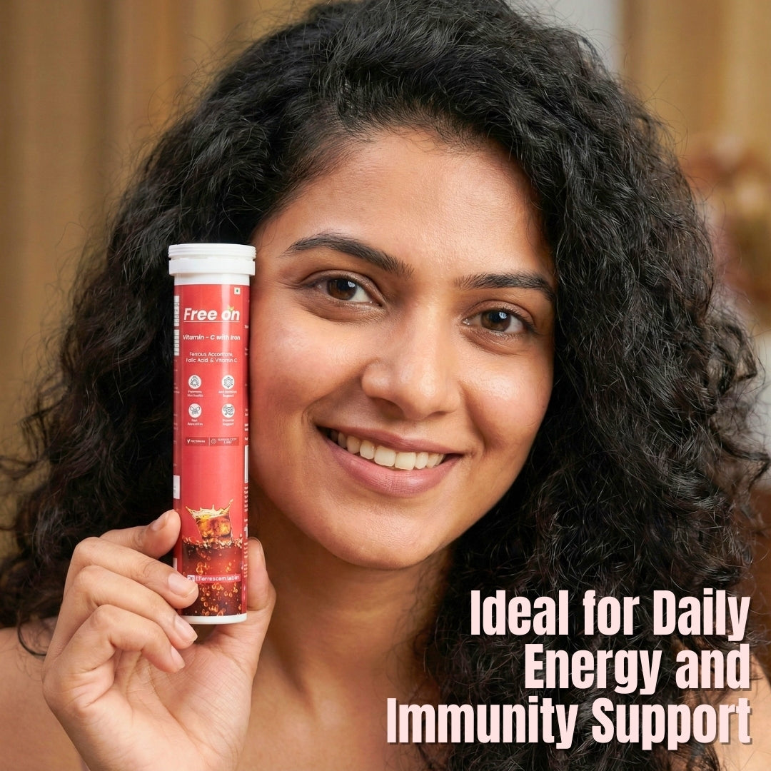 An Indian woman with curly dark hair smiles as she holds a tube of Free On Vitamin C with Iron effervescent tablets. The red tube features illustrations of bubbles and is labeled "Ideal for Daily Energy and Immunity Support."